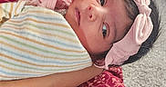 Sitara is registered to the contest to win money with this photo: baby, infant, child, blanket, headband, pink_bow, hand, arm, person, fabric, pattern, red_clothing, striped_blanket, indoor, carpet, portrait, cute, newborn, soft_lighting, holding