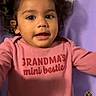 Sitara is registered to the contest to win money with this photo: toddler, child, curly_hair, pink_shirt, text_on_clothing, purple_blanket, lying_down, face, portrait, cute, indoors, baby, smiling, young_child, person, infant, casual_photo, phone_screenshot, clothing, expression