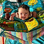baby, child, smiling, play_seat, toy, colorful, indoor, happy, face, curly_hair, infant, bright, patterned, seat, arms, fabric, cute, cheerful, playful, young