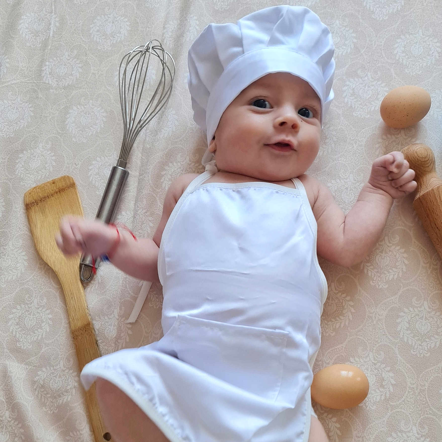 Filip a rejoint le concours — aidez-le/la à gagner de superbes lots ! apron, baby, chef_hat, child, cooking_theme, cute, eggs, indoors, infant, kitchen_utensils, lying_down, patterned_background, playful, portrait, rolling_pin, small_hands, smiling, whisk, white_clothing, wooden_spatula