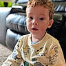 bright_eyes, casual_clothing, child, couch, curious, curly_hair, cute, dinosaur, expression, face, home, indoor, living_room, person, portrait, seated, soft_lighting, sweater, toddler, young_child