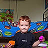 John Paul is registered to the contest to win money with this photo: bed, black_tshirt, blanket, boy, building_blocks, carpet, casual, child, colorful, floor, furniture, indoor, mario, playing, red_hair, room, smiling, toy, tv, wall