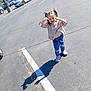 child, girl, smiling, parking_lot, shadow, sunny, jeans, pigtails, sneakers, asphalt, cars, playful, outdoor, casual_clothing, daytime, cute, happy, person, fun, bunny_patches