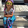 accessory, casual, child, colorful_dress, fun, girl, green_glasses, happy, outdoor, patterned_clothing, person, playful, portrait, purple, sitting, smile, sunlight, tiara, wooden_steps, young