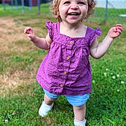 Charlotte is registered to the contest to win money with this photo: toddler, child, smiling, outdoor, grass, purple_clothing, denim_shorts, white_shoes, curly_hair, happy, walking, daylight, fence, lawn, young_child, cute, sunny, person, nature, playful
