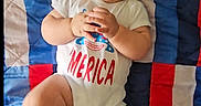 Ezra joined the competition — help win amazing prizes! baby, child, infant, smiling, laughing, onesie, clothing, blanket, quilt, colorful, red, blue, white, happy, cute, playful, person, portrait, indoor, skin