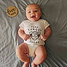 baby, infant, smiling, onesie, park_ranger, wooden_sign, five_months, lying_down, blanket, cute, happy, child, human, skin, head, arms, legs, feet, indoors, portrait