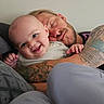 Ezra is registered to the contest to win money with this photo: baby, man, tattoo, smile, hug, couch, indoor, person, head, face, happy, relax, family, affection, skin, clothing, beard, adult, baby_clothes, casual
