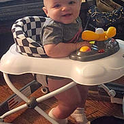 Ezra is registered to the contest to win money with this photo: baby, walker, indoor, smiling, child, floor, toy, footwear, sock, clothing, person, furniture, seat, play, happy, head, face, leg, wood_floor, home