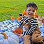 toddler, child, smiling, outdoor, grass, blanket, pumpkin, plush_toy, leaves, fall, autumn, curly_hair, striped_shirt, overalls, black_shoes, playful, nature, toy_mushrooms, happy, portrait