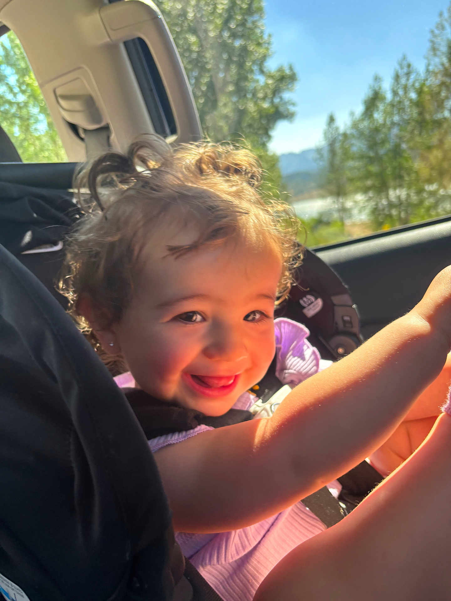 Brexlee joined the competition — help win amazing prizes! toddler, child, car_seat, smiling, curly_hair, sunlight, window, trees, mountains, car_interior, happy, portrait, seatbelt, playful, daylight, nature, face, person, clothing, travel