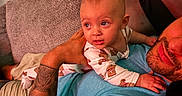 Sophie is registered to the contest to win money with this photo: baby, man, tattoo, couch, blanket, indoor, relaxing, child, person, home, toddler, clothing, portrait, face, skin, arm, hand, fabric, furniture, living_room