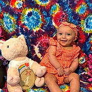 Sophie joined the competition — help win amazing prizes! baby, child, infant, smiling, plush_toy, pig, orange_clothing, headband, tie_dye_blanket, milestone, wooden_plaque, sitting, cute, happy, indoors, colorful, portrait, person, fabric, toy