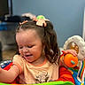 child, toddler, girl, smiling, happy, portrait, indoor, playroom, activity_center, baby_toy, orange_toy, colorful, hair_bow, long_hair, sitting, t_shirt, highland_cow, playful, childhood, family_photo