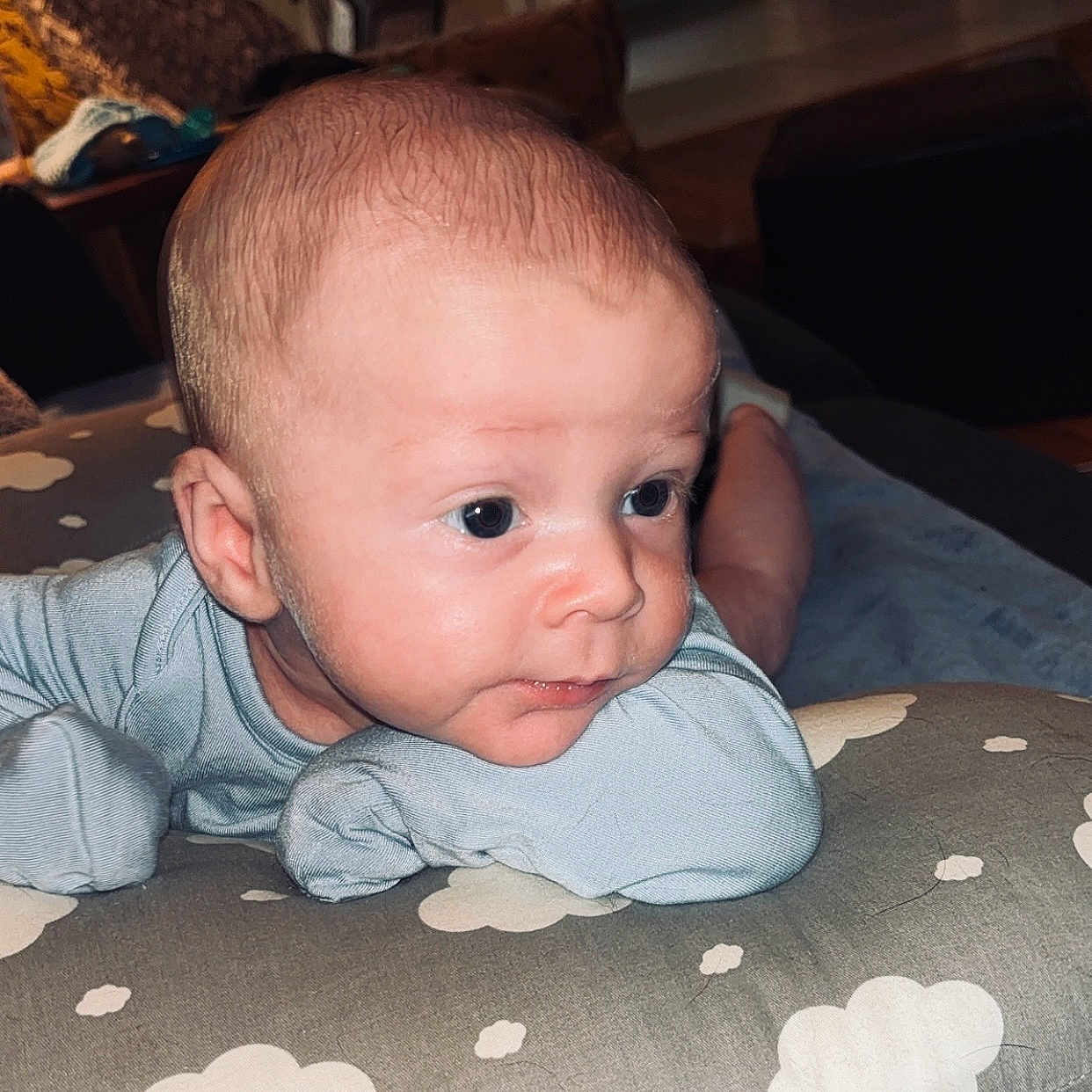Miles is registered to the contest to win money with this photo: baby, blanket, blue_outfit, child, clothing, cloud_pattern, curious, eyes, face, furniture, head, home, indoors, infant, pillow, resting, skin, small_hands, soft_lighting, toddler