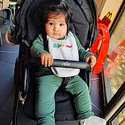Youness Ben Mena participe au concours pour gagner de l'argent avec cette photo : baby, bib, black_stroller, chair, child, cute, expression, face, floor, green_clothing, hair, hand, indoor, infant, person, safety_bar, sitting, stroller, white_socks, window