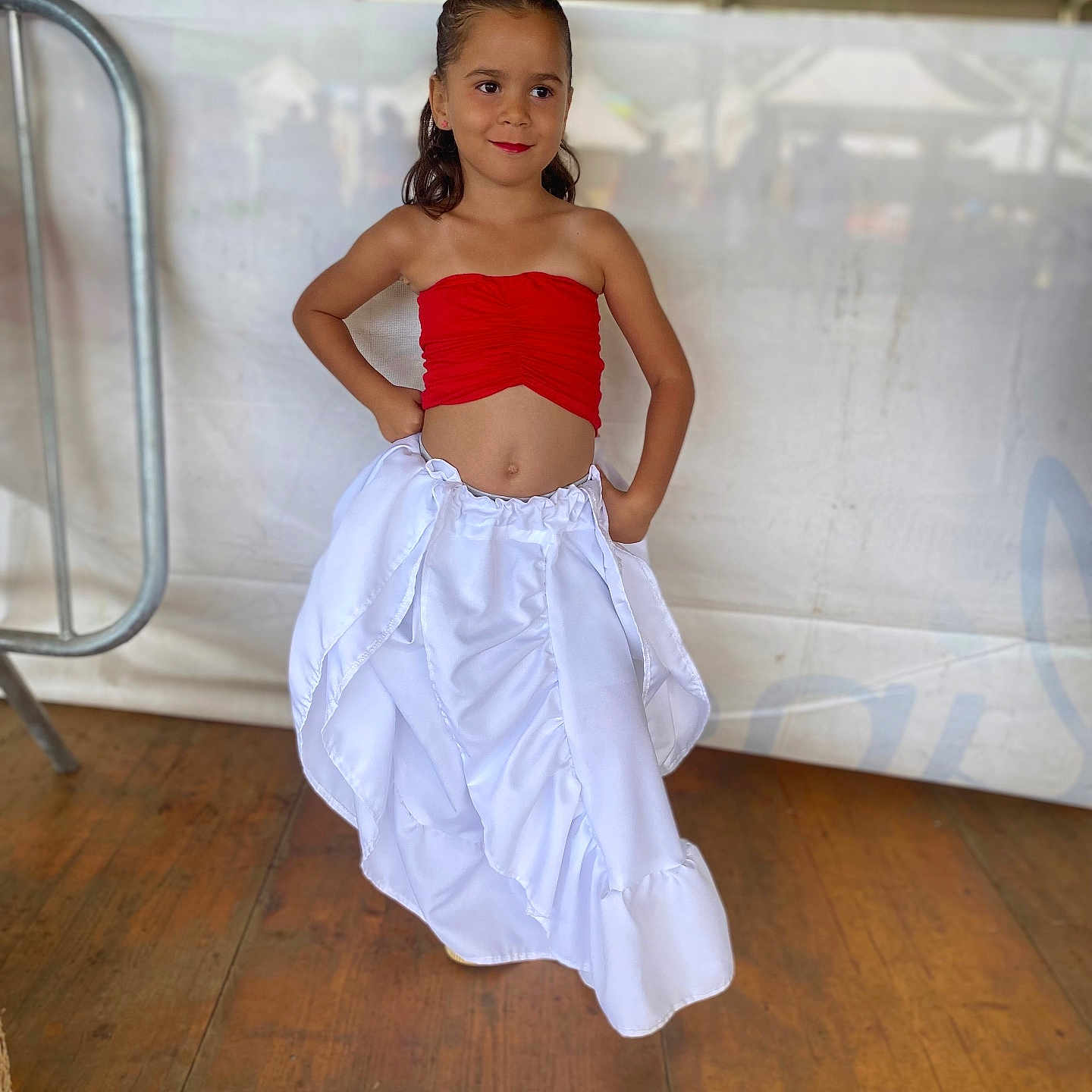 Marie participe au concours pour gagner de l'argent avec cette photo : child, colorful_clothing, confident, cute, event, fashion, girl, hands_on_hips, happy, indoors, long_hair, portrait, posing, red_top, smiling, standing, tent, white_skirt, wooden_floor, young