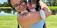 Lady Mae is registered to the contest to win money with this photo: woman, dog, glasses, blue_dress, outdoor, grass, lake, sky, clouds, sunny, happy, hug, pet, nature, smile, tattoo, animal, summer, portrait, friendship