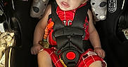 Remmi is registered to the contest to win money with this photo: baby, car_seat, infant, red_clothing, black_straps, warning_labels, cushion, indoor, child, footwear, black_shoes, socks, toy, secure, seat_belt, head_support, close_up, portrait, young_child, baby_boy