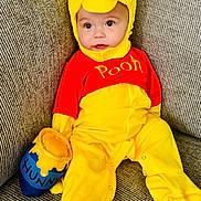 Sutton is registered to the contest to win money with this photo: baby, child, costume, yellow, red, winnie_the_pooh, plush, honey_pot, sofa, couch, seated, cute, indoor, face, clothing, footwear, happy, portrait, infant, soft_toy
