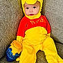 baby, child, costume, yellow, red, winnie_the_pooh, plush, honey_pot, sofa, couch, seated, cute, indoor, face, clothing, footwear, happy, portrait, infant, soft_toy