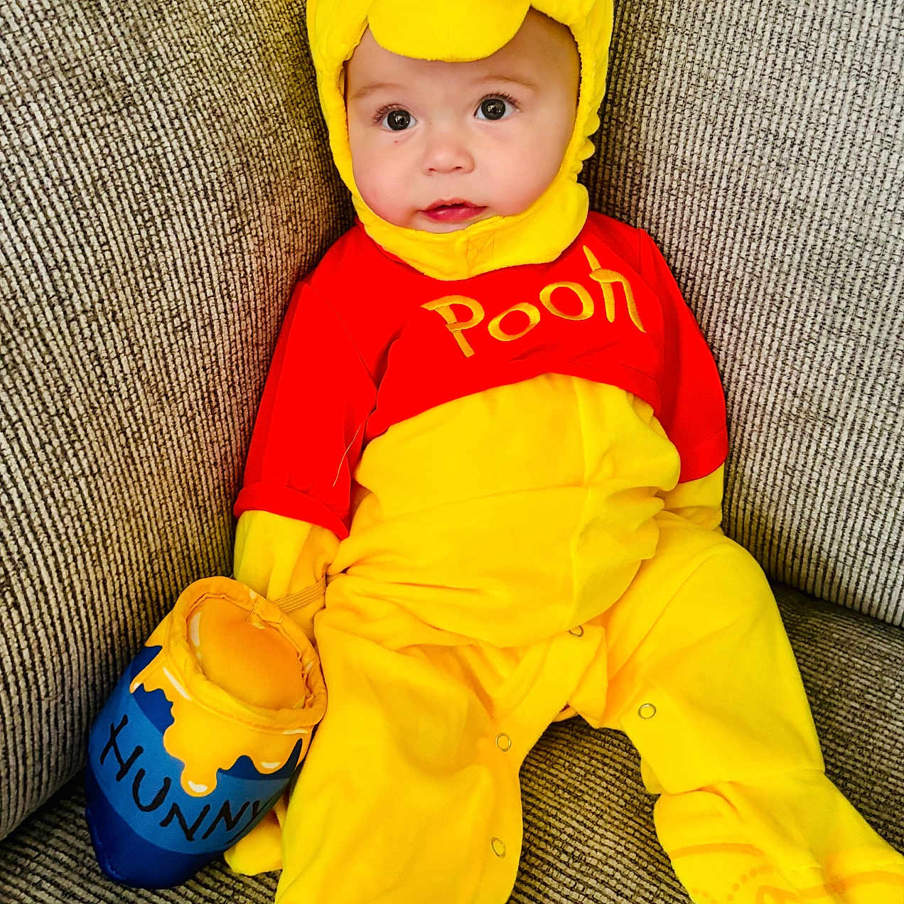 Sutton is registered to the contest to win money with this photo: baby, child, clothing, costume, couch, cute, face, footwear, happy, honey_pot, indoor, infant, plush, portrait, red, seated, sofa, soft_toy, winnie_the_pooh, yellow