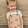 child, toddler, smile, overall, elephant_print, striped_shirt, brick_wall, standing, happy, cute, blond_hair, short_hair, casual_clothing, outdoor, portrait, person, young_child, fashion, playful, innocent