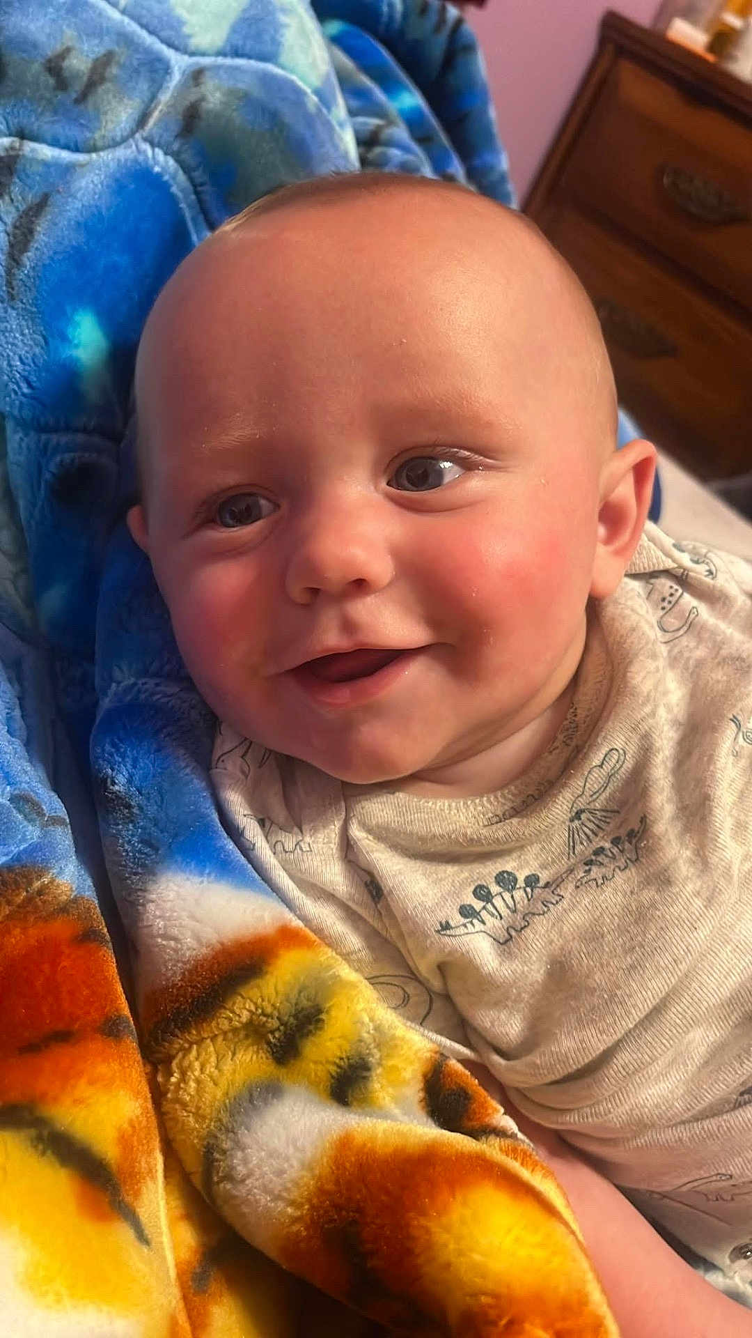 Kane is registered to the contest to win money with this photo: baby, smiling, blanket, blue, orange, face, infant, cute, portrait, closeup, indoors, child, happy, cozy, fabric, bedroom, person, skin, clothing, head