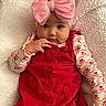 baby, child, infant, pink_bow, red_dress, blanket, cute, portrait, face, hand, soft_texture, cozy, young_child, clothing, headwear, lying_down, indoors, adorable, expression, person