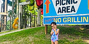 Aakifa is registered to the contest to win money with this photo: child, girl, swimsuit, water_slide, picnic_area_sign, grass, outdoor, playground, summer, trees, park, smiling, posing, daylight, nature, footwear, sandals, fun, recreation, summer_fun