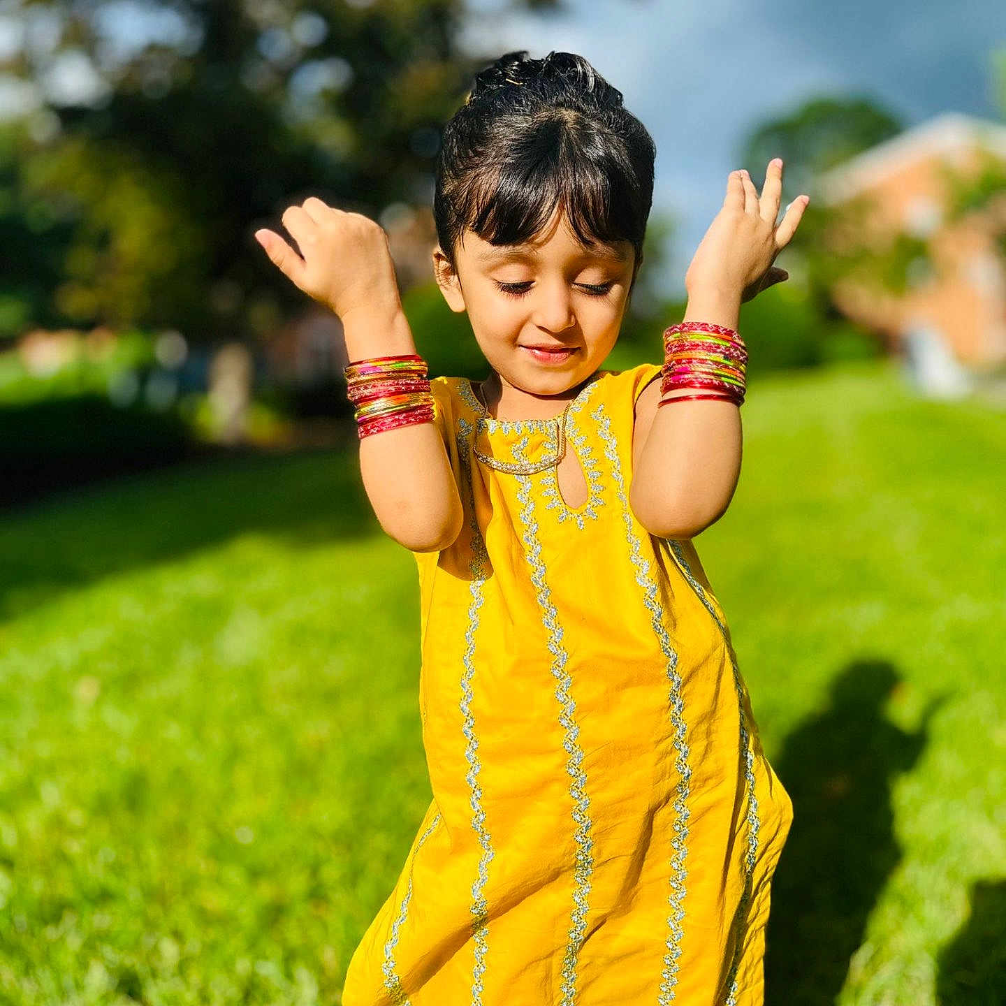 Aakifa is registered to the contest to win money with this photo: background_blur, bracelets, child, closed_eyes, daylight, fashion, grass, greenery, happy, nature, outdoor, person, playful, portrait, shadow, smiling, sunlight, traditional_clothing, yellow_dress, young