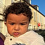 Ismaël a rejoint le concours — aidez-le/la à gagner de superbes lots ! child, toddler, curly_hair, white_shirt, embroidery, outdoor, daylight, portrait, serious_expression, face, person, building, sky, sunlight, shadow, urban, window, clothing, head, close_up