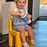 Zachary joined the competition — help win amazing prizes! toddler, child, yellow_chair, overalls, socks, indoor, wooden_floor, plastic_chair, blonde_hair, cup, smiling, casual_clothing, playing, door, floor_mat, home_interior, young_child, seated, curious_expression, light