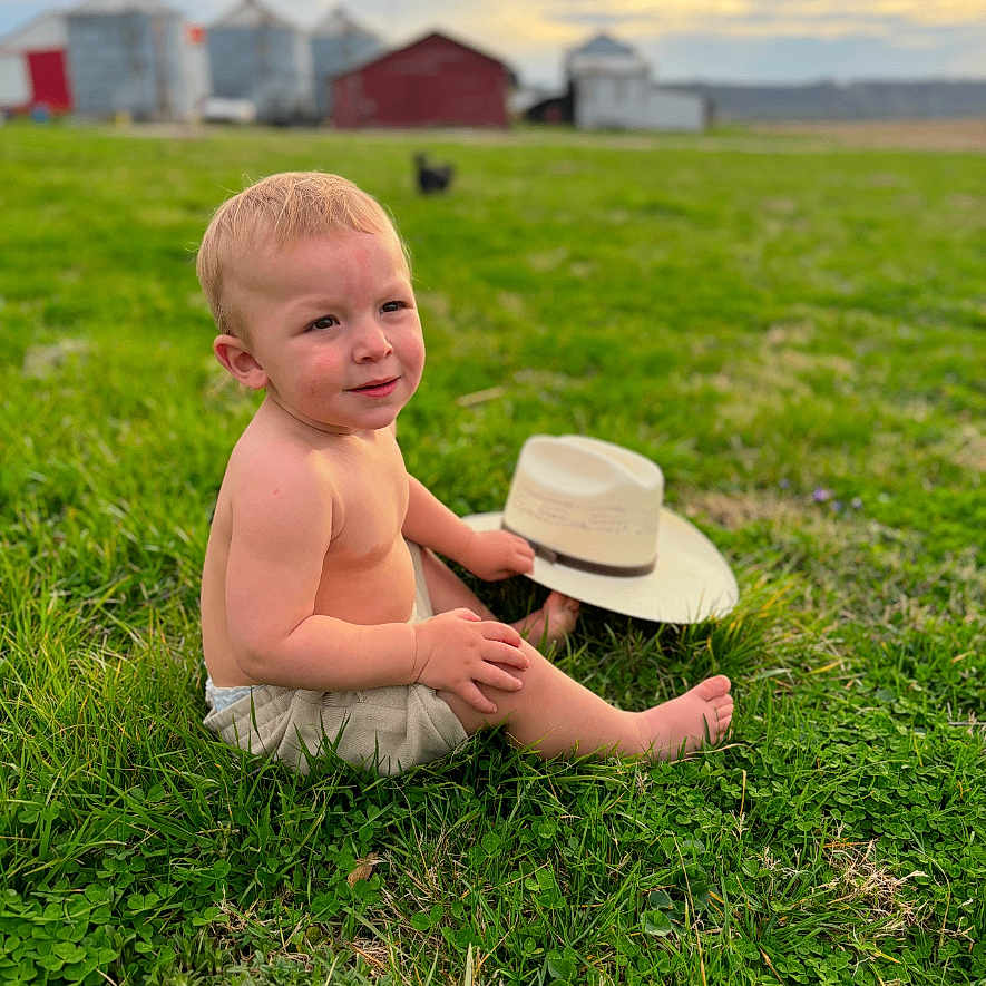 Oliver is registered to the contest to win money with this photo: baby, bodypart, clothing, cowboyhat, face, finger, grass, hand, hat, head, lawn, nature, outdoors, person, photography, plant, portrait, sitting, summer, sunhat