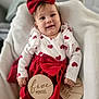 baby, infant, child, smiling, red_bow, heart_pattern, dress, white_blanket, wooden_sign, five_months, cute, portrait, indoor, happy, young_child, headband, sitting, person, milestone, cozy