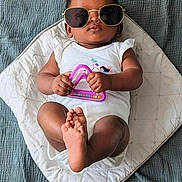 Bryan joined the competition — help win amazing prizes! baby, child, sunglasses, toy, white_clothing, cushion, blanket, indoor, portrait, infant, cute, relaxed, person, feet, hand, face, fashion, accessory, playful, laying_down