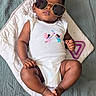 baby, infant, sunglasses, white_onesie, fairy_print, blanket, quilted, blue_green_bedspread, cute, relaxed, portrait, indoors, child, fashion, accessory, feet, hands, laying_down, cool, adorable