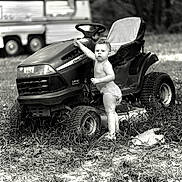 Atlus is registered to the contest to win money with this photo: toddler, child, lawn_tractor, john_deere, diaper, grass, outdoor, vehicle, black_and_white, nature, person, standing, summer, rural, small_child, play, curious, portrait, wheel, camper