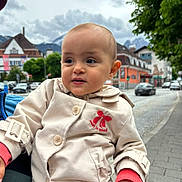 Emma participe au concours pour gagner de l'argent avec cette photo : toddler, child, coat, red_bow, outdoor, street, buildings, cloudy_sky, mountains, sidewalk, cars, tree, curious, person, urban, daytime, casual_clothing, portrait, hand, expression
