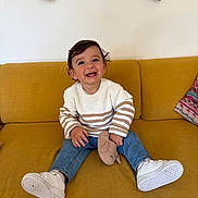 Lissandro a rejoint le concours — aidez-le/la à gagner de superbes lots ! toddler, child, smiling, sitting, couch, yellow_couch, white_sneakers, striped_sweater, blue_jeans, soft_toy, happy, indoor, curly_hair, cute, casual_clothing, playful, portrait, home, furniture, cozy