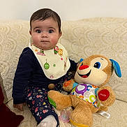 Lyna participe au concours pour gagner de l'argent avec cette photo : baby, child, plush_toy, pacifier, bib, couch, patterned_fabric, heart_pattern, sitting, indoor, cute, smiling_toy, colorful, soft_toy, infant, clothing, sock, face, person, toy