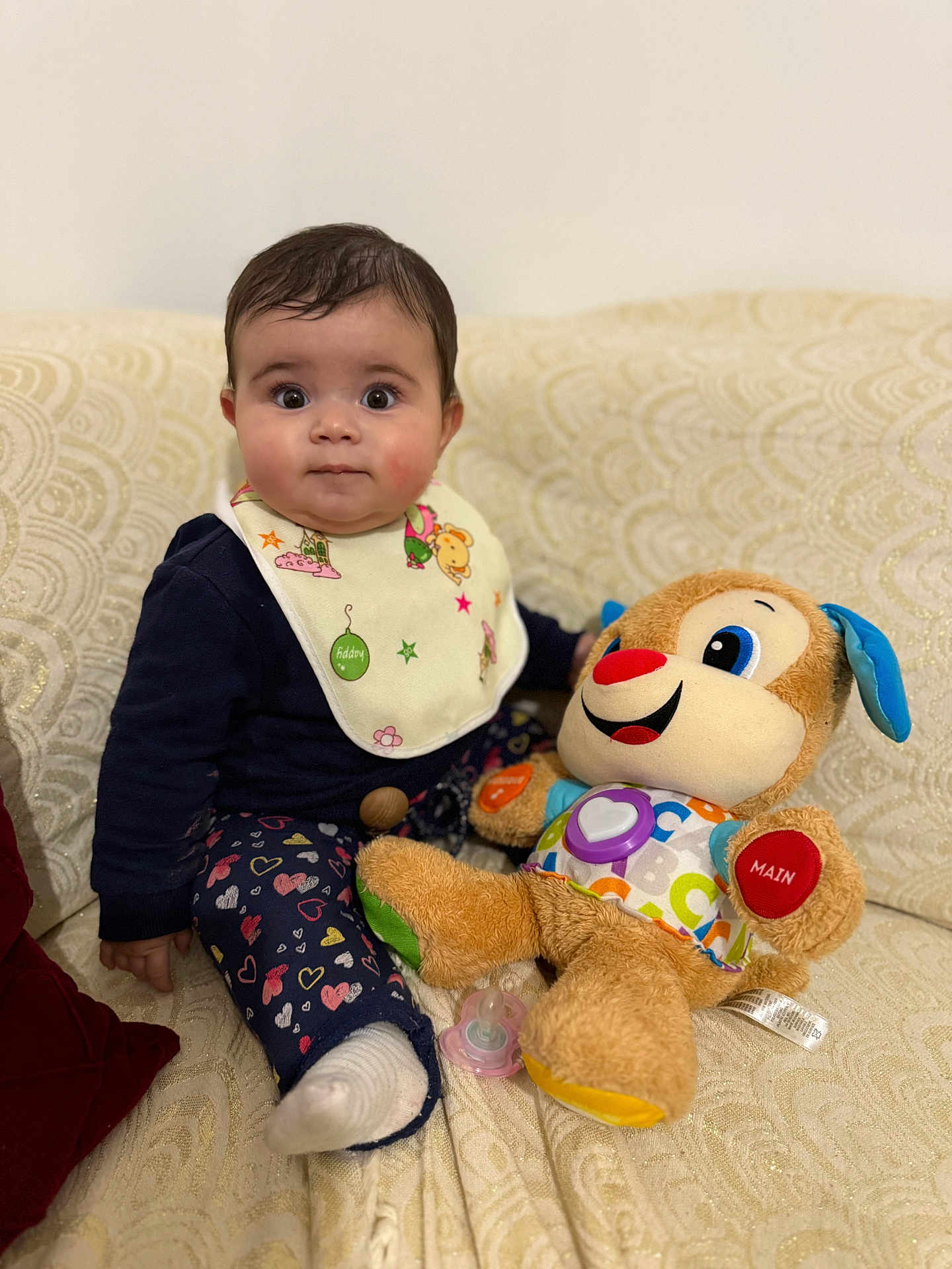 Lyna participe au concours pour gagner de l'argent avec cette photo : baby, child, plush_toy, pacifier, bib, couch, patterned_fabric, heart_pattern, sitting, indoor, cute, smiling_toy, colorful, soft_toy, infant, clothing, sock, face, person, toy