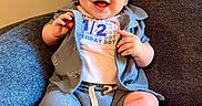 Clay is registered to the contest to win money with this photo: baby, boy, smiling, happy, sitting, blue_armchair, clothing, shirt, shorts, infant, cute, celebration, half_birthday, indoors, portrait, child, feet, hands, face, warm_lighting