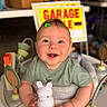 Clay is registered to the contest to win money with this photo: activity_center, baby, blue_eyes, blurred_background, bunny_toy, child, cute, face, garage_sale, green_shirt, hands, happy, home, indoor, infant, person, play, sign, smiling, toy