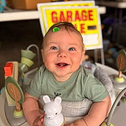 Clay is registered to the contest to win money with this photo: activity_center, baby, background, bunny, child, clothing, cute, eyes, face, garage_sale, green_shirt, hands, happy, indoor, infant, play, portrait, sign, smiling, toy