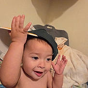 Bryan is registered to the contest to win money with this photo: toddler, child, baby, cap, hat, indoor, blanket, smile, happy, cute, gesture, person, skin, face, hand, expression, cozy, bedroom, playful, young