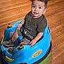 Bryan is registered to the contest to win money with this photo: blue, child, cute, floor, happy, indoor, light, looking_up, person, play, seat_belt, shorts, smiling, sneakers, toddler, toy_car, tshirt, vehicle, wooden_floor, yellow