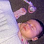 baby, sleeping, blanket, knitted, pacifier, pacifier_clip, beads, pink, heart_pattern, infant, child, cute, resting, floor, carpet, hand, face, calm, indoors, soft_lighting
