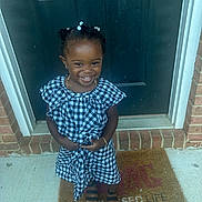 Jada joined the competition — help win amazing prizes! child, girl, smiling, dress, black_and_white, checkered, sandals, door, welcome_mat, bracelet, necklace, hair_beads, outdoor, concrete, brick, happy, standing, portrait, young, fashion