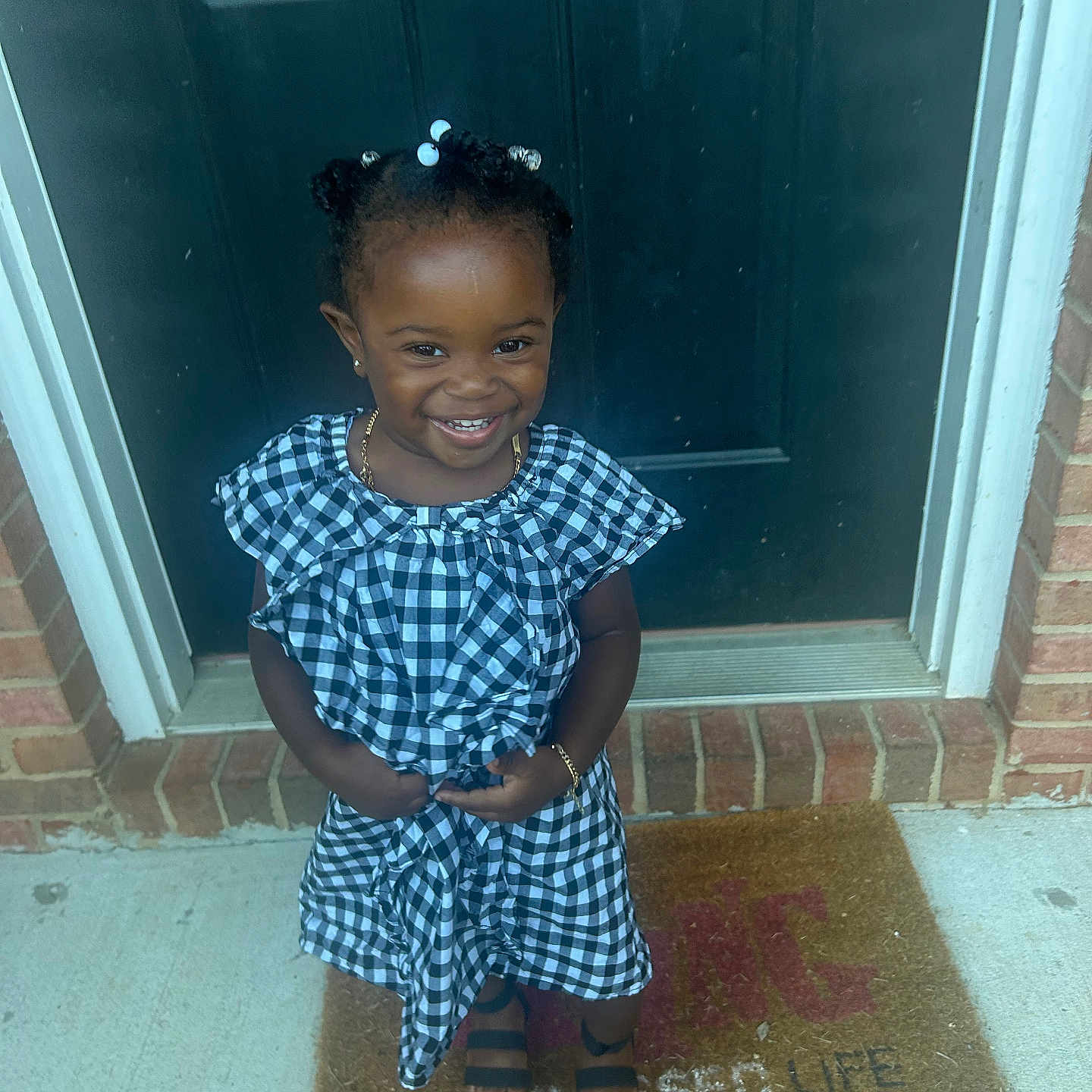 Jada joined the competition — help win amazing prizes! black_and_white, bracelet, brick, checkered, child, concrete, door, dress, fashion, girl, hair_beads, happy, necklace, outdoor, portrait, sandals, smiling, standing, welcome_mat, young